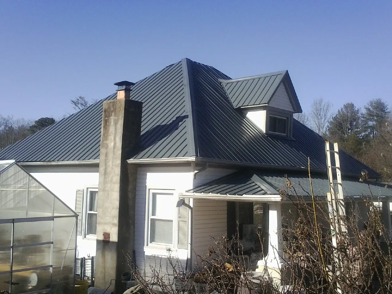 Dark blue standing seam metal roof on a white farmhouse with dormer in Sublime