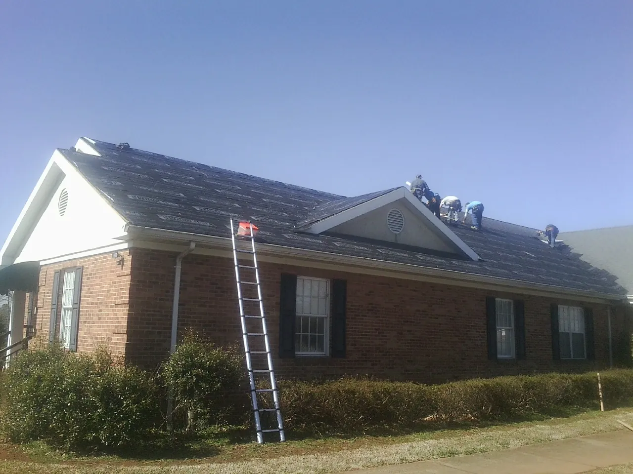 Crew tearing shingles off a brick ranch roof with a ladder set — Metal Roof Repair work by our crew in Sublime