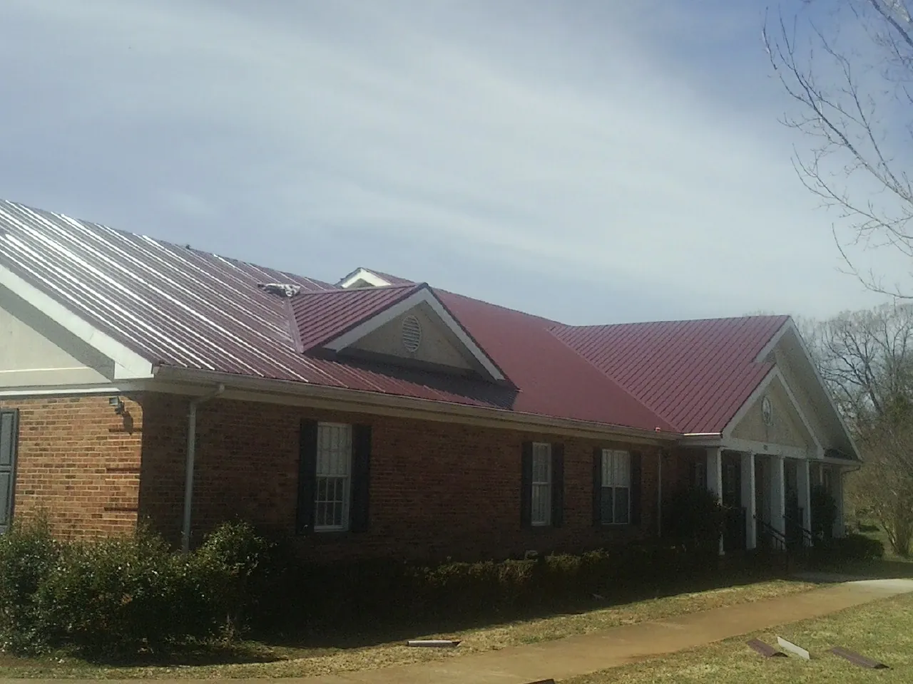 Red metal roof with gabled entries on a long brick building, from a Hail Damage Roof Repair job in Sublime
